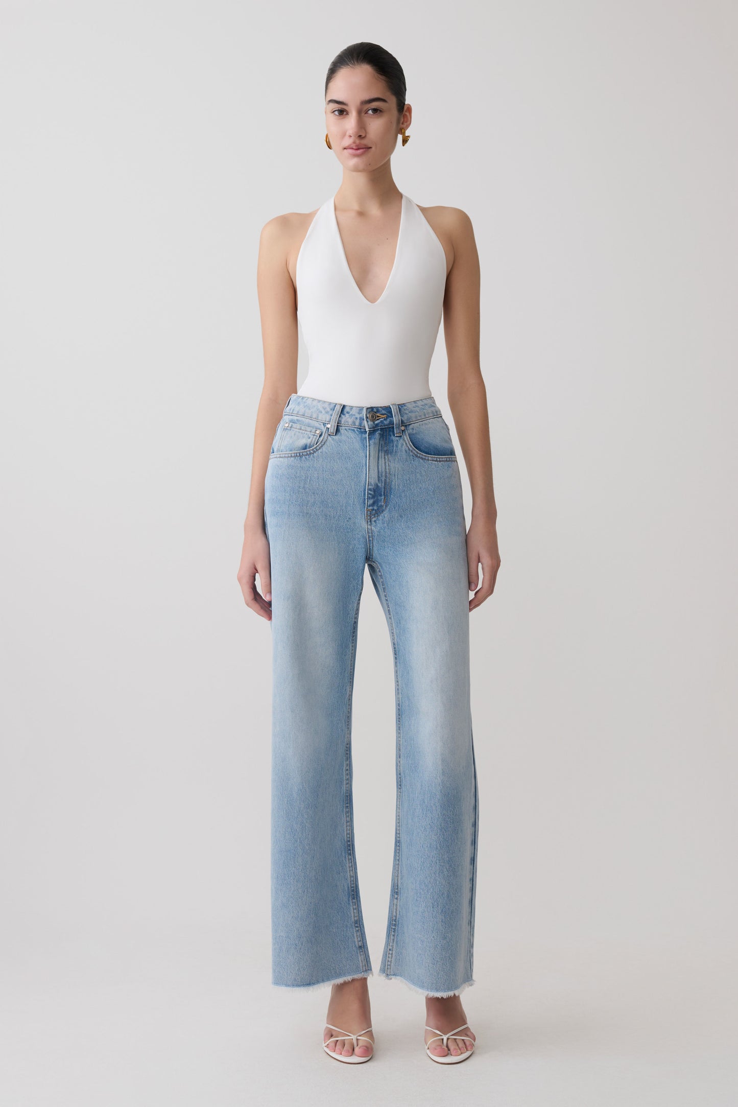 Woman wearing a white slinky halter bodysuit with blue jeans.
