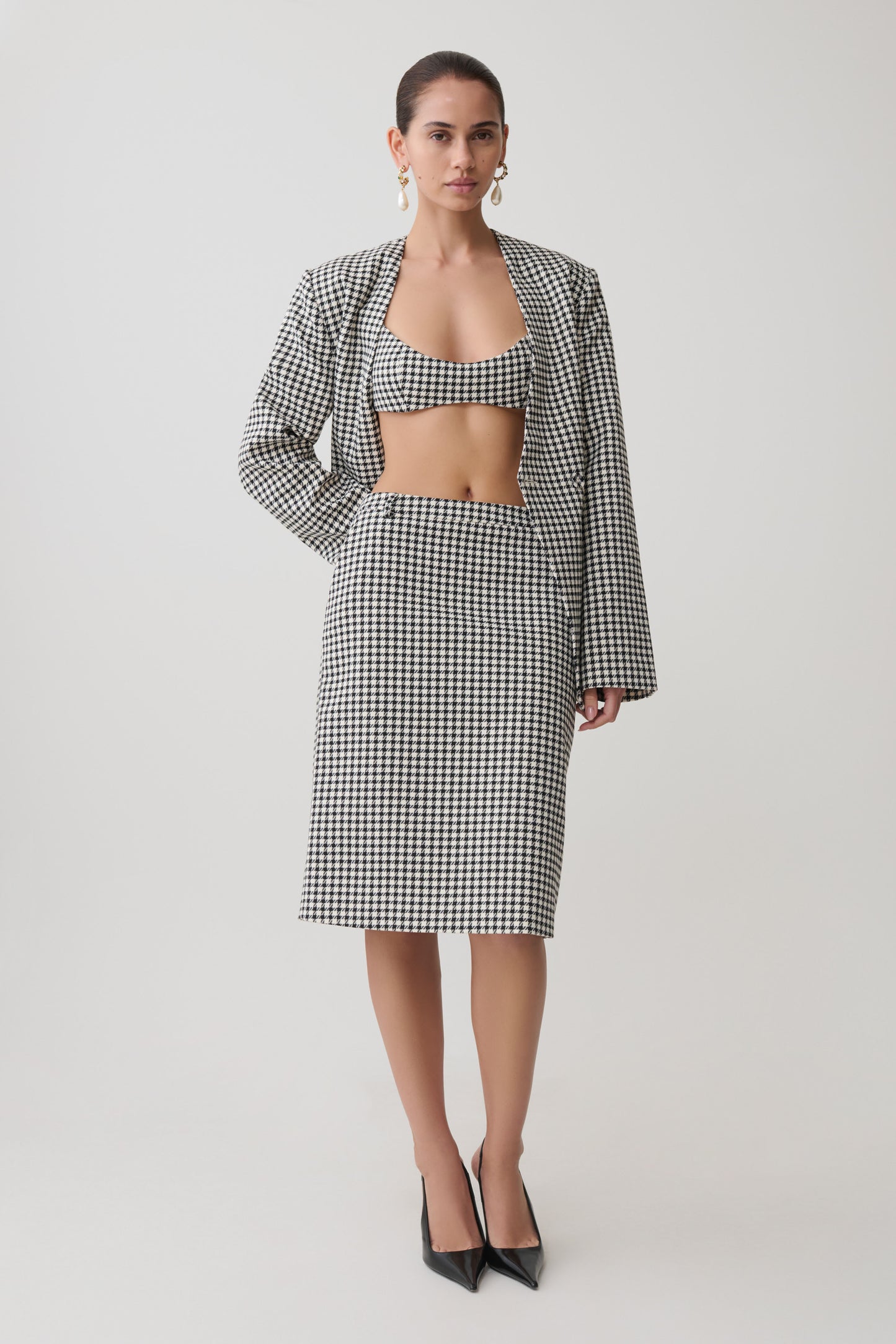 Woman wearing a black and white tweed checkered bralette with matching blazer and midi skirt.