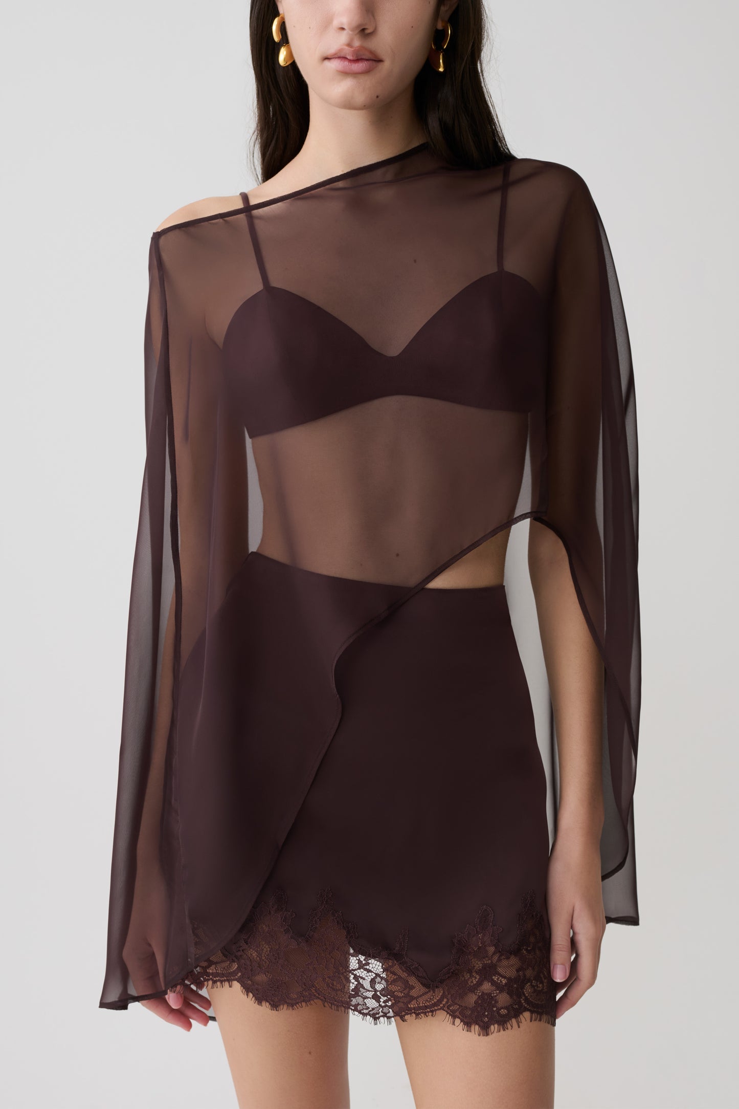 Woman wearing brown bralette with chiffon cape with matching lace and satin mini skirt.