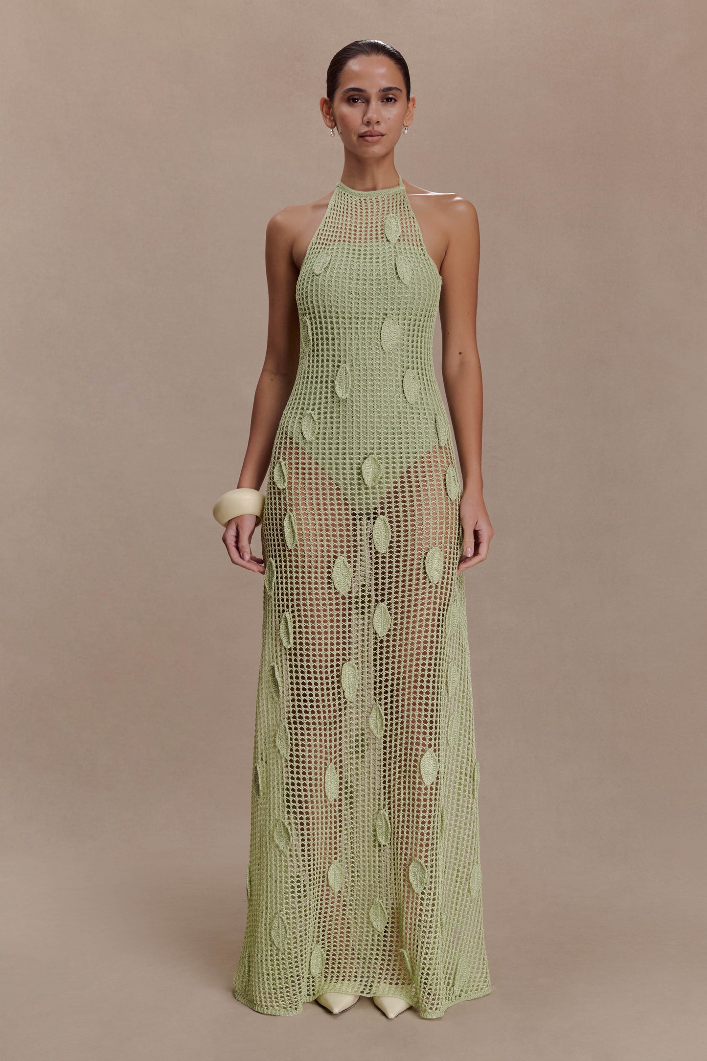 Woman wearing a sheer green crochet halter maxi dress with intricate leaf detailing.