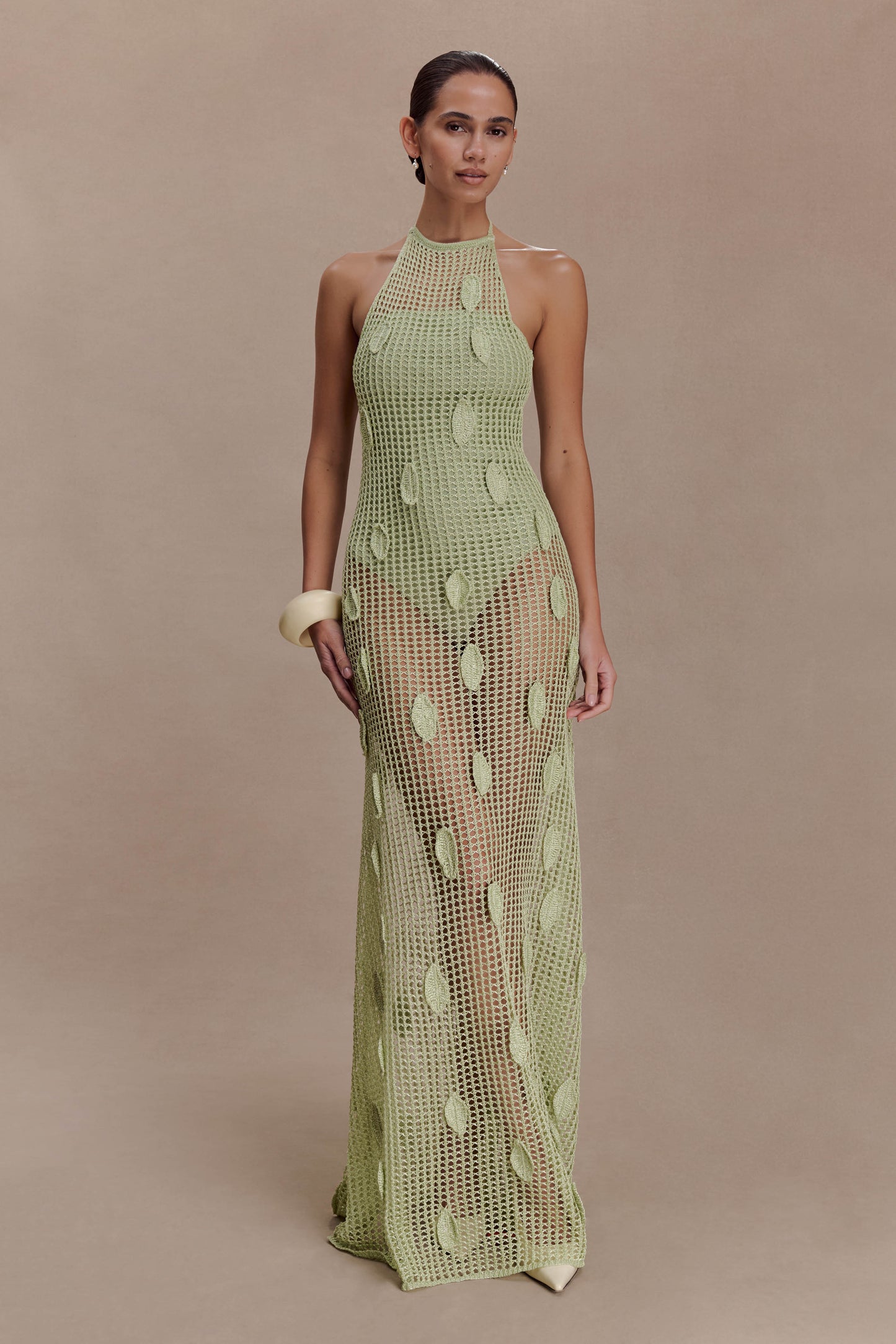 Woman wearing a sheer green crochet halter maxi dress with intricate leaf detailing.