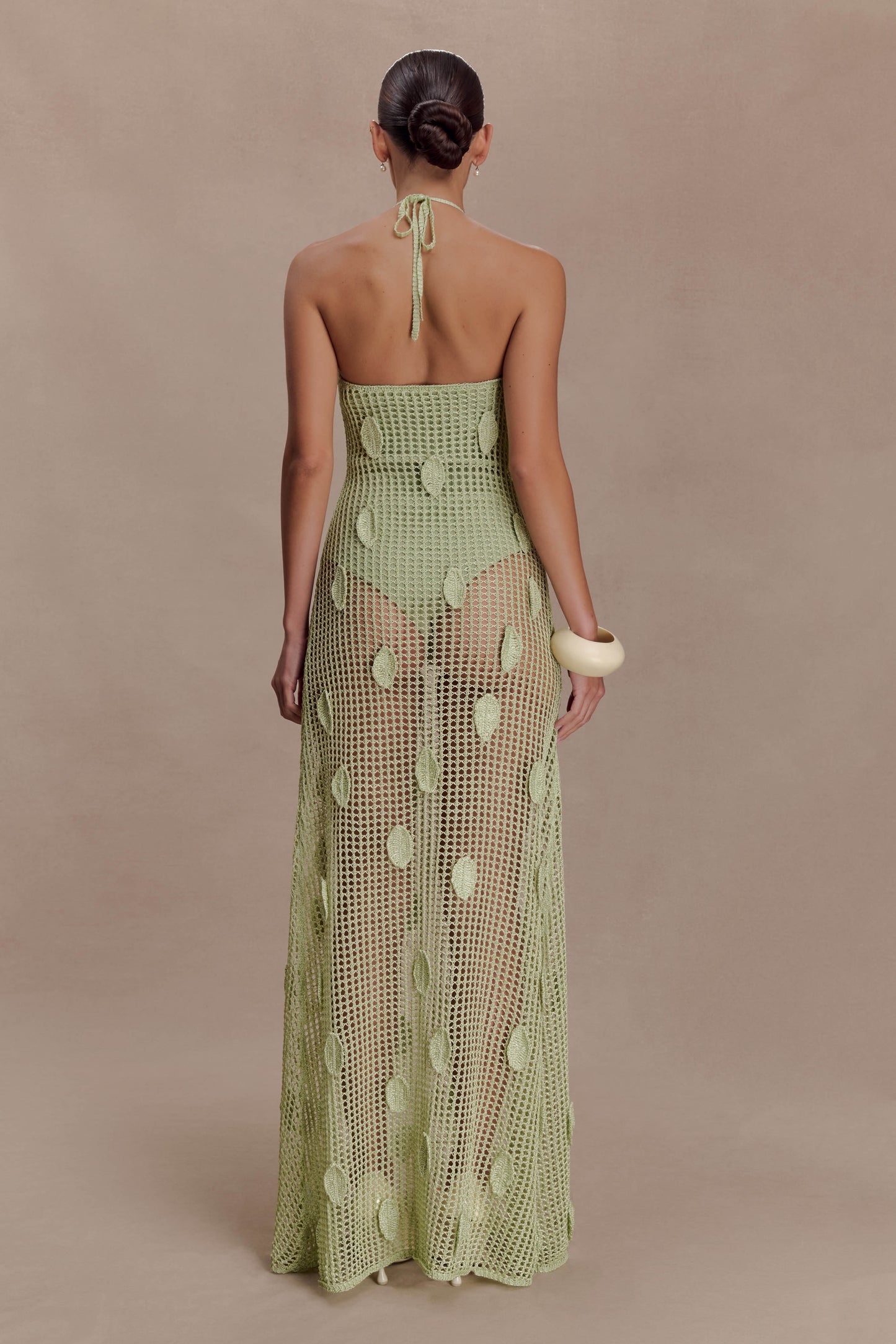 Woman wearing a sheer green crochet halter maxi dress with intricate leaf detailing.