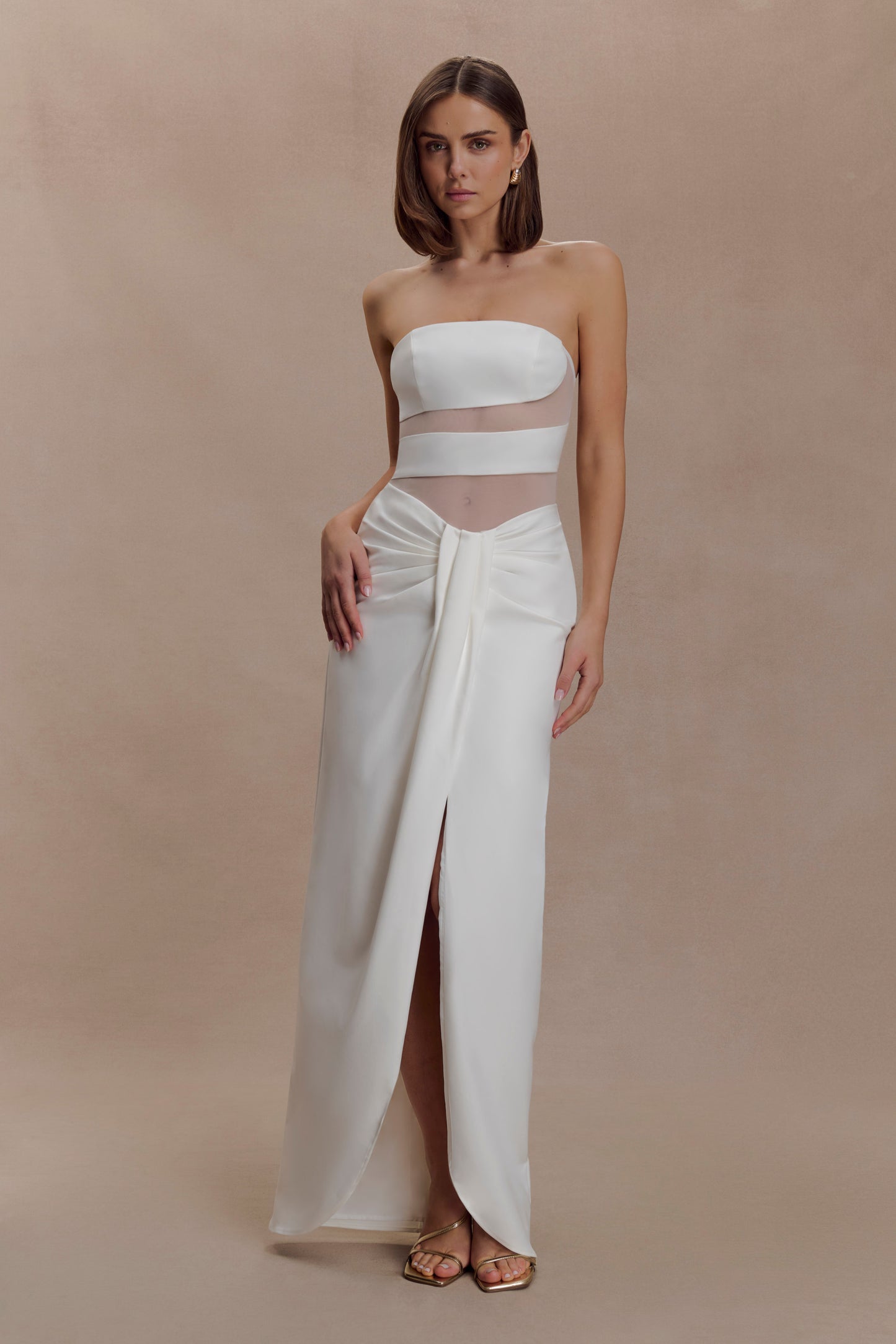 Woman wearing a white strapless top and long white skirt against a beige background