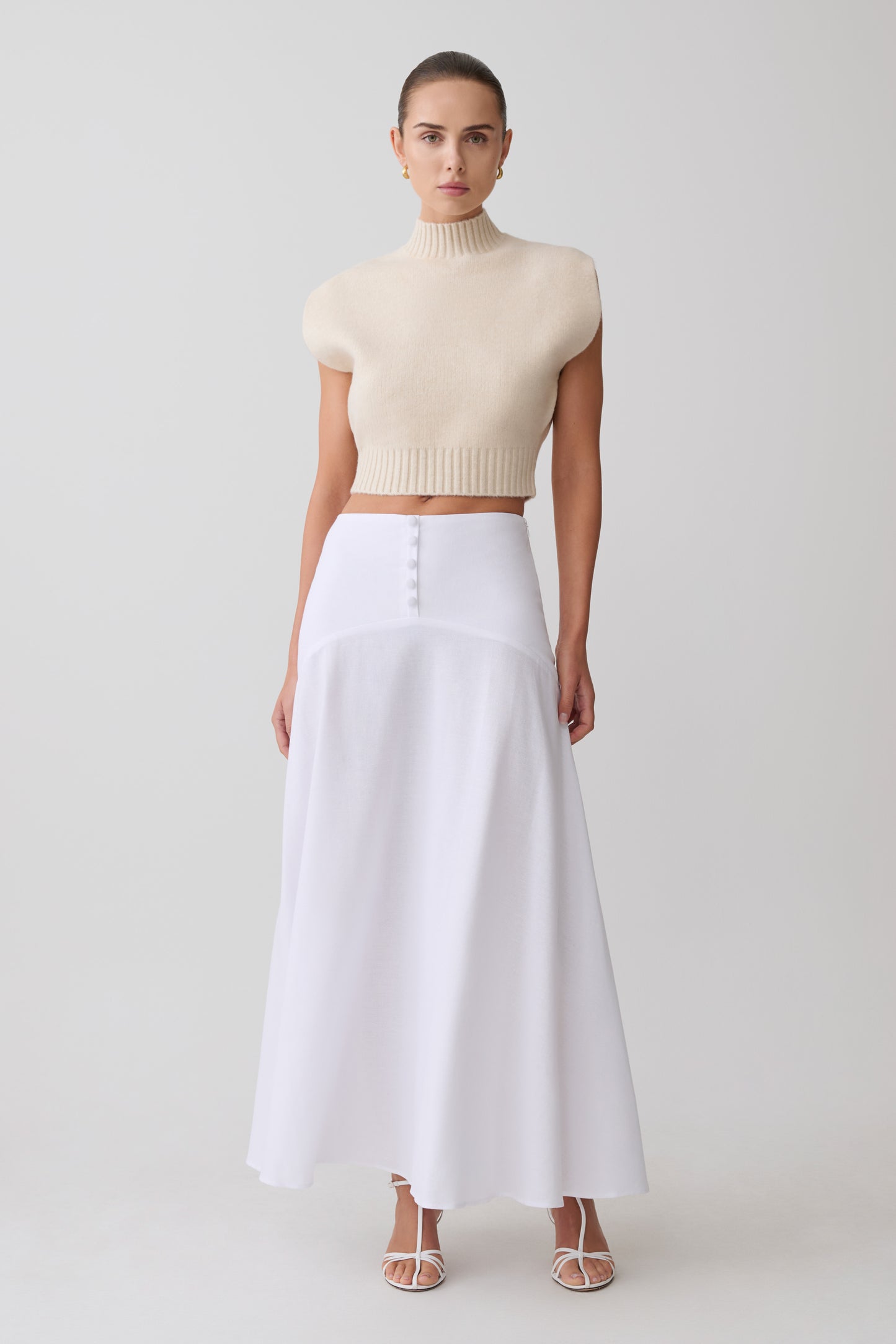 Woman wearing a beige turtleneck top and white skirt on a light gray background
