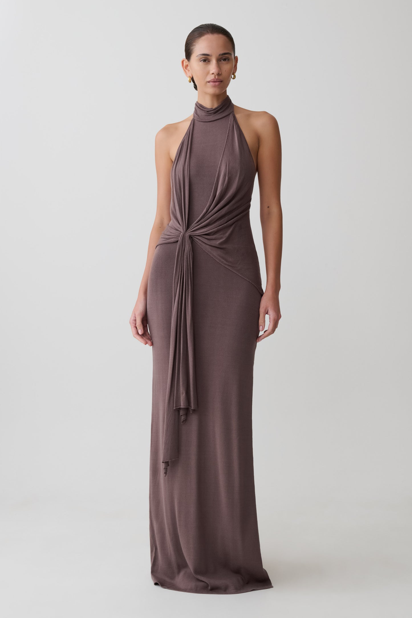 Woman wearing a long brown dress with a halter neck design on a white background