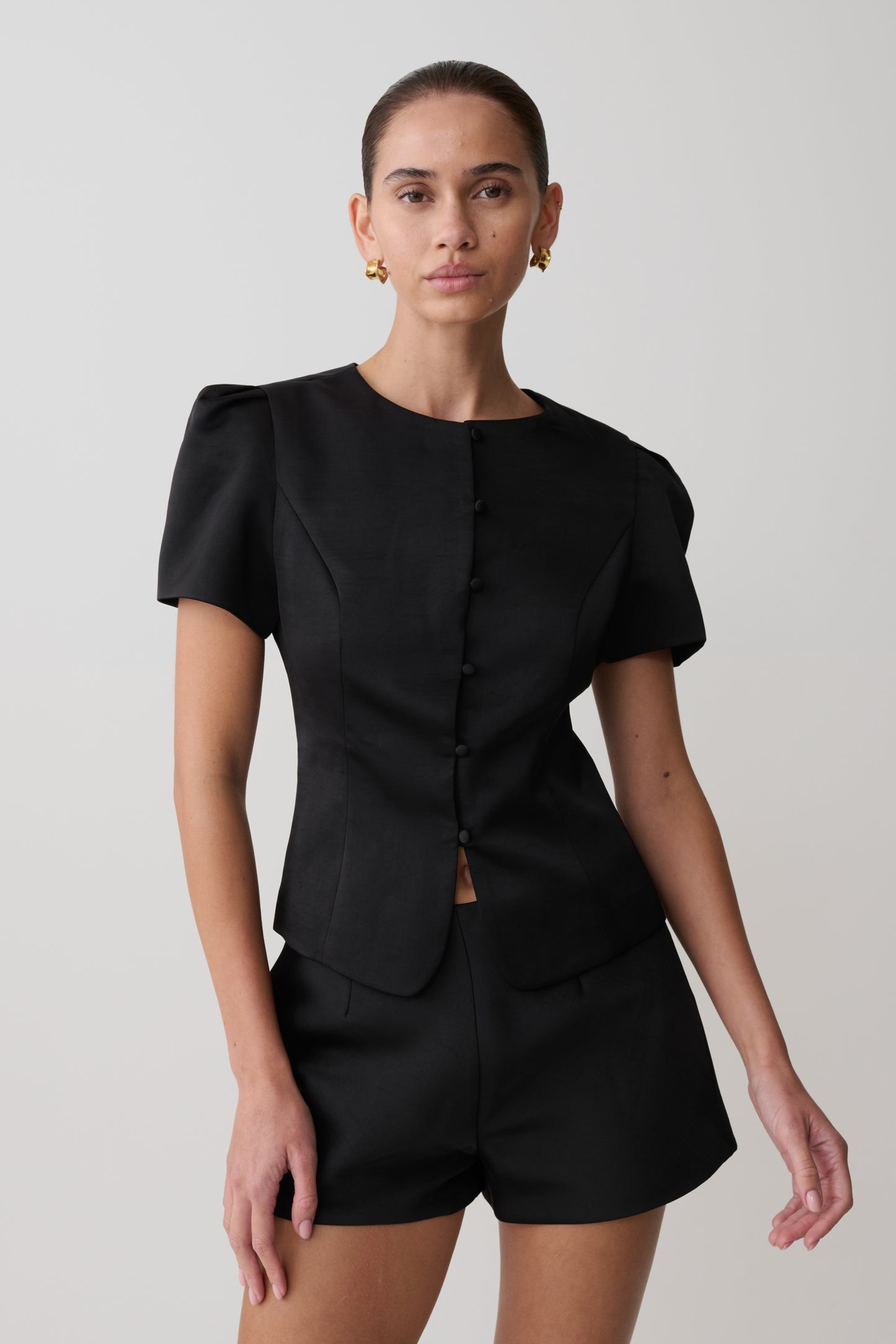 Woman wearing a black outfit with puffed sleeves on a plain background