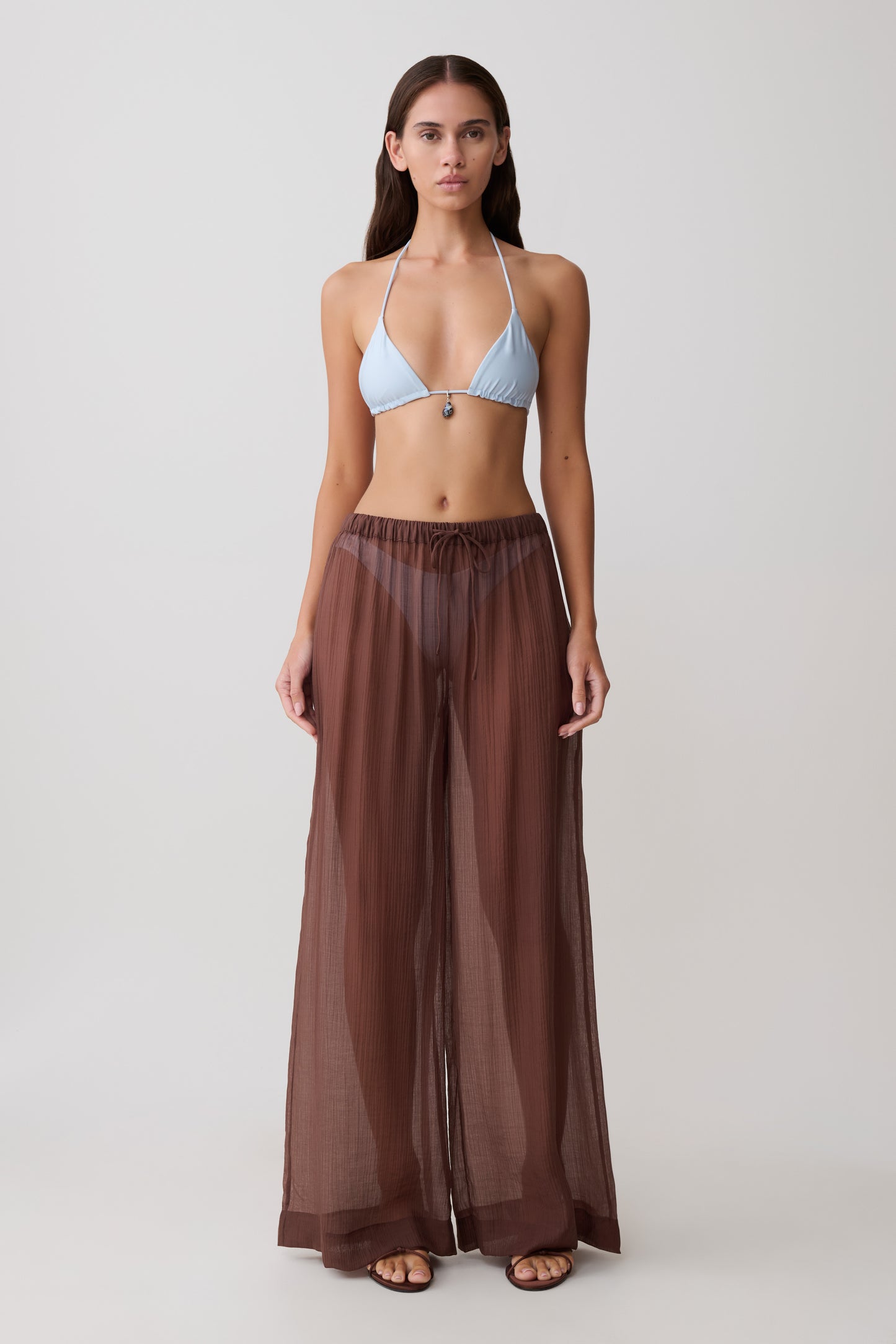 Woman wearing a light blue bikini top and sheer brown drawstring wide pants.