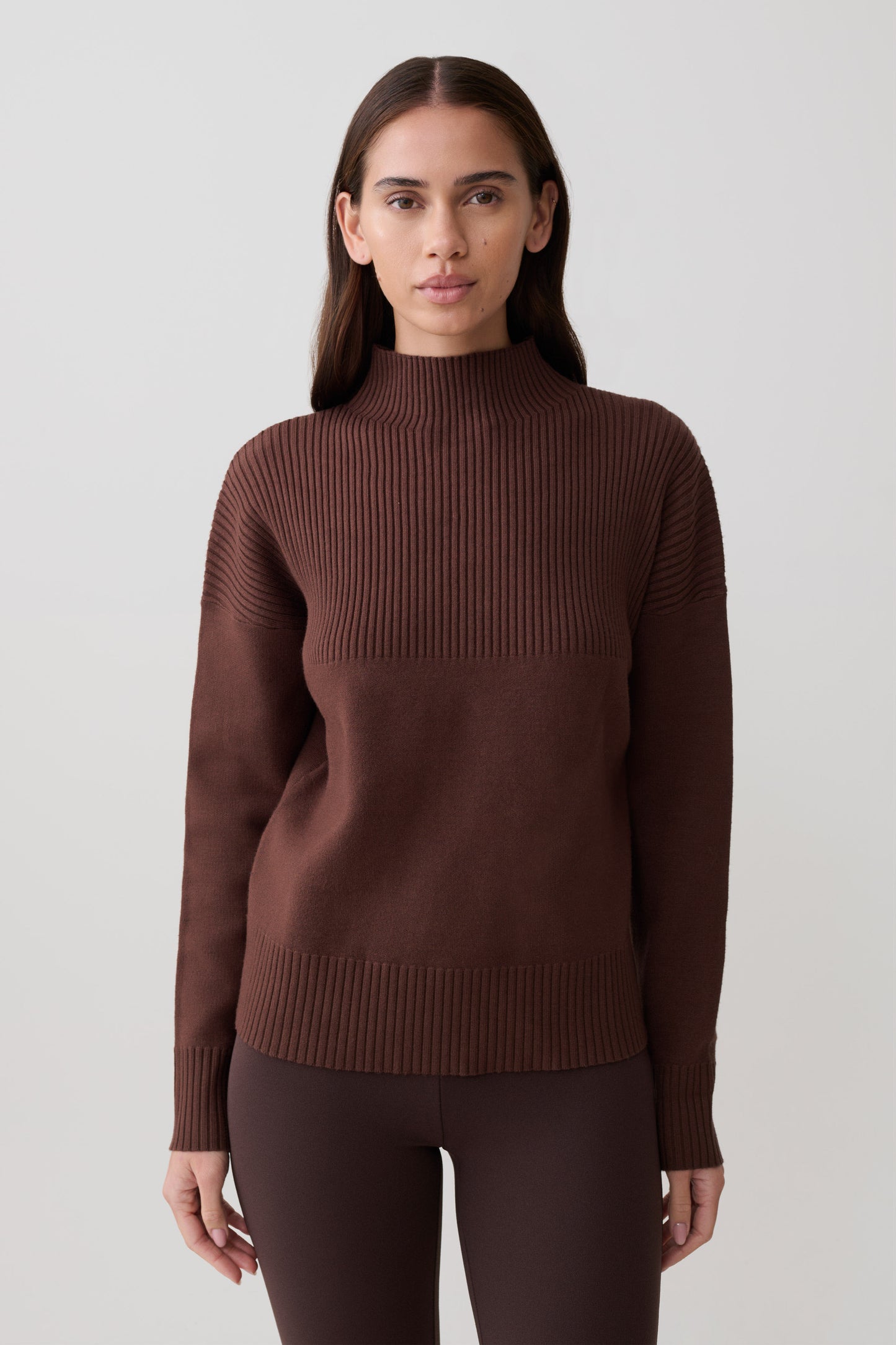 Woman wearing a brown ribbed hgih neck sweater.