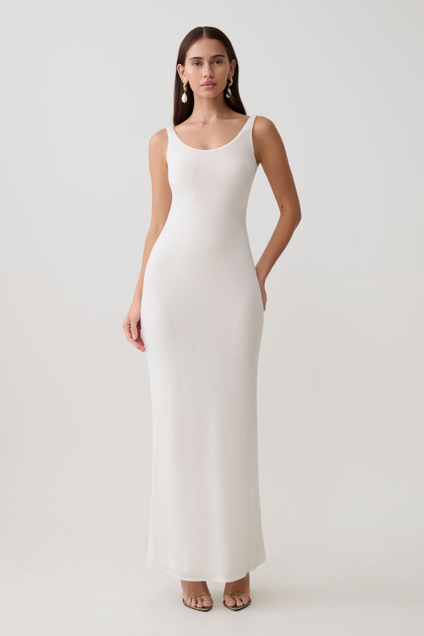 Woman wearing a white scoop neck jersey maxi dress.