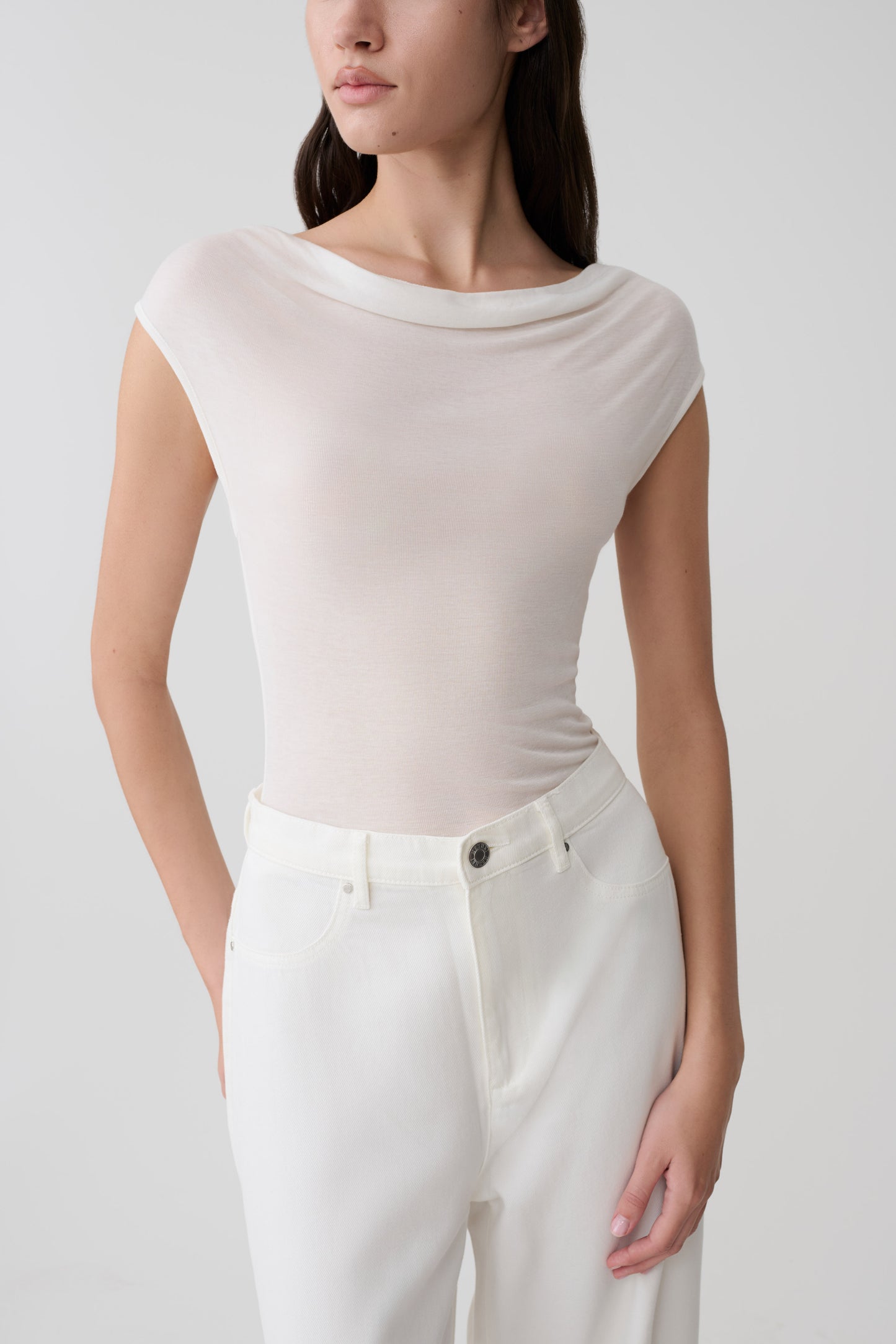 Woman wearing a white sleeveless sheer top and white pants.