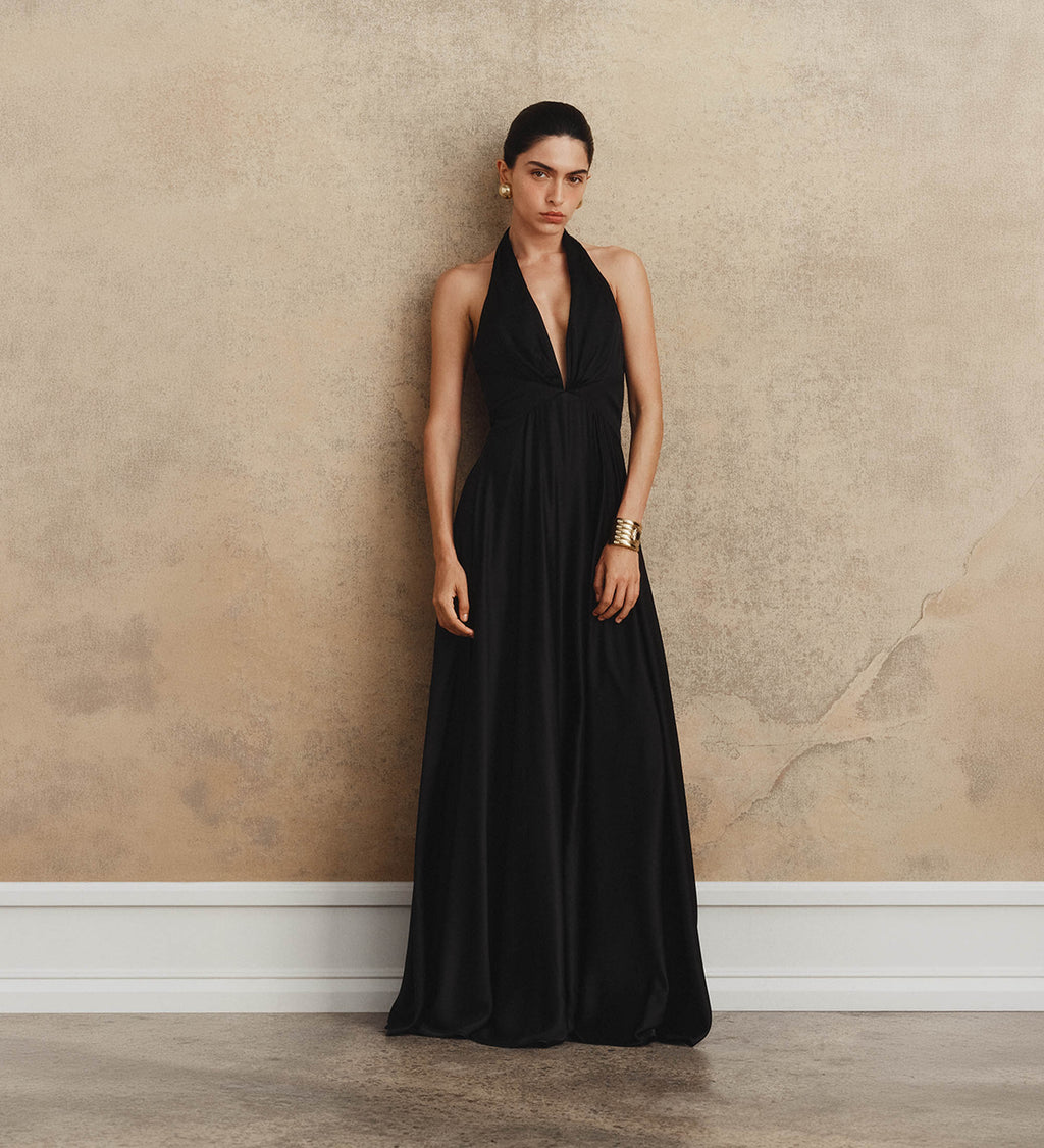 Woman wearing a black halter neck dress against a textured beige wall.