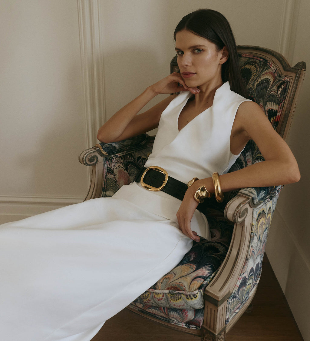 Woman in a white dress with a black belt sitting on an ornate chair.
