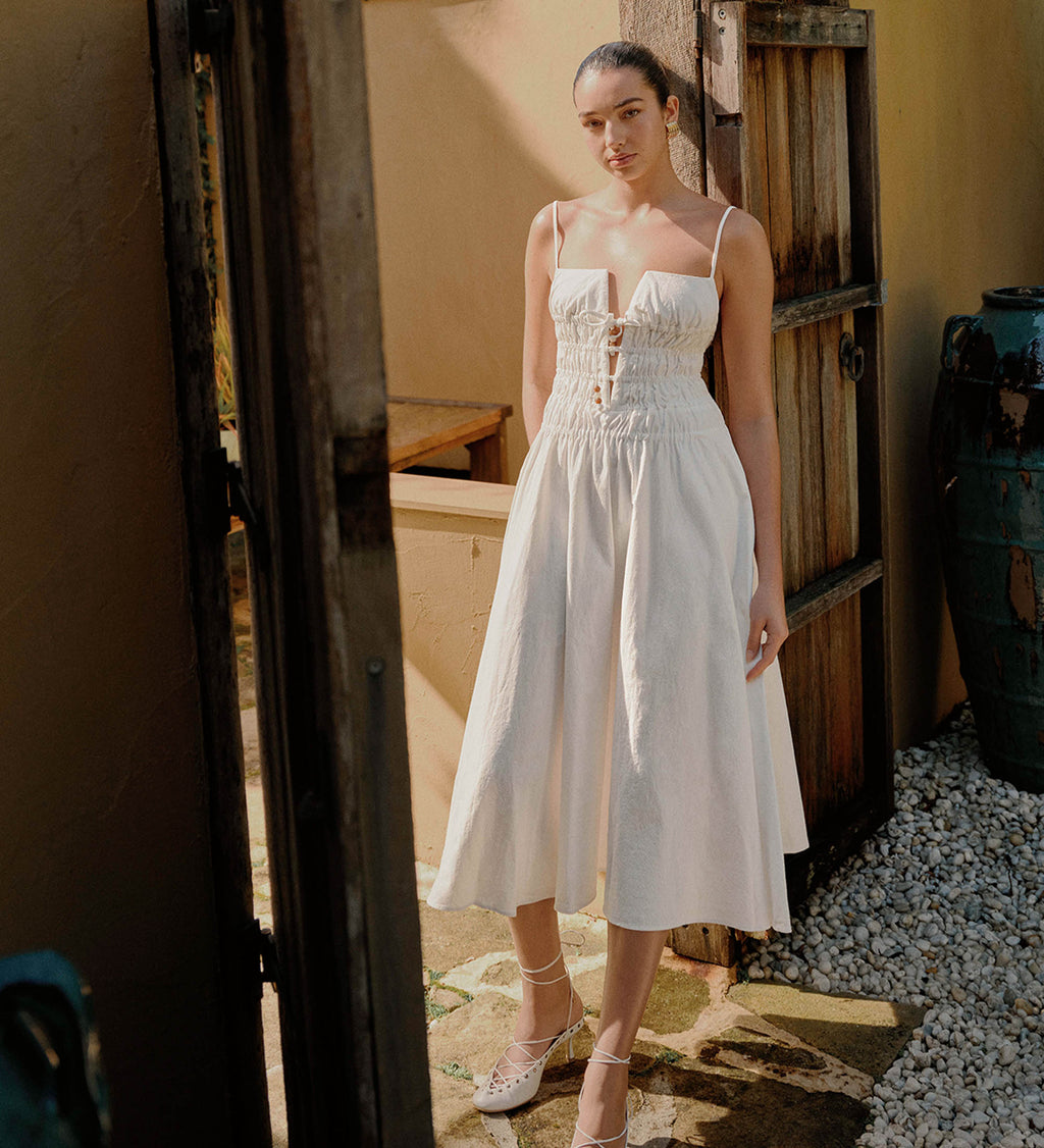 Woman in a white dress standing in a rustic outdoor setting.