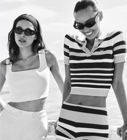 Two women wearing sunglasses and summer clothing on a beach.