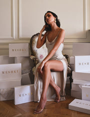 Image of woman wearing a satin slit maxi dress sitting between gift boxes