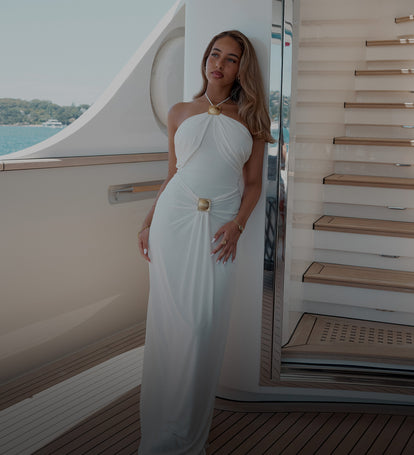 Woman in a white dress on a yacht deck with ocean view.