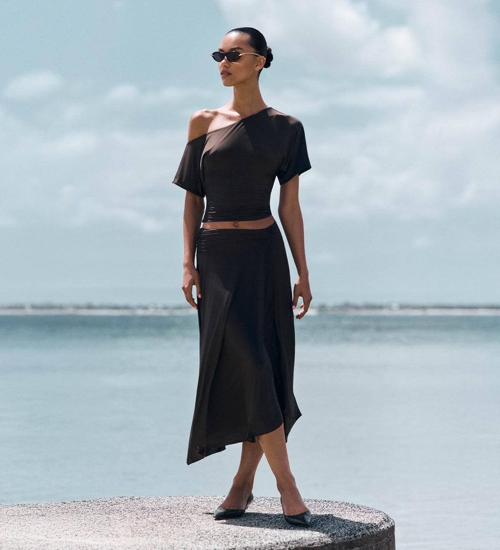 Woman in front of ocean wearing matching brown top and skirt