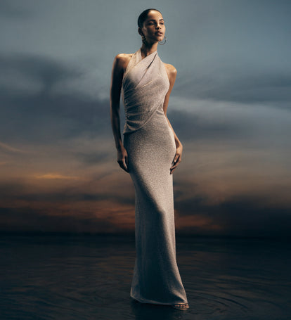 Woman in a silver dress standing in water with a dramatic sky.