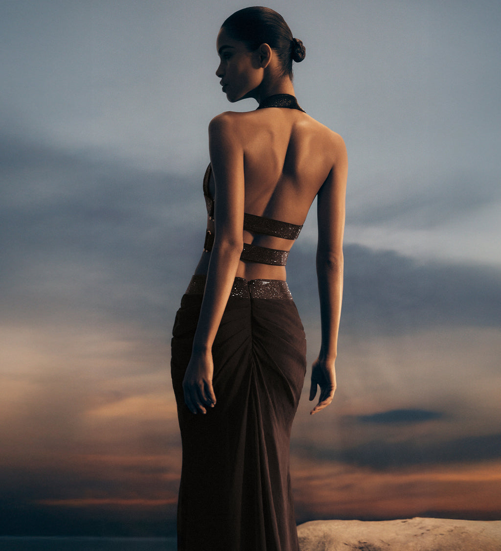 Woman in a dark set standing against a dramatic sky.
