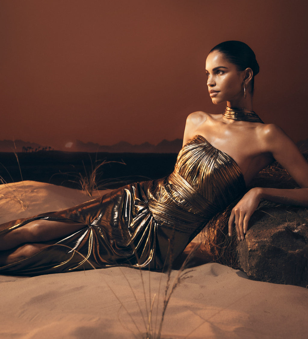 Woman in a gold dress sitting in a desert landscape.