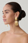 Woman wearing gold textured statement drop earrings.