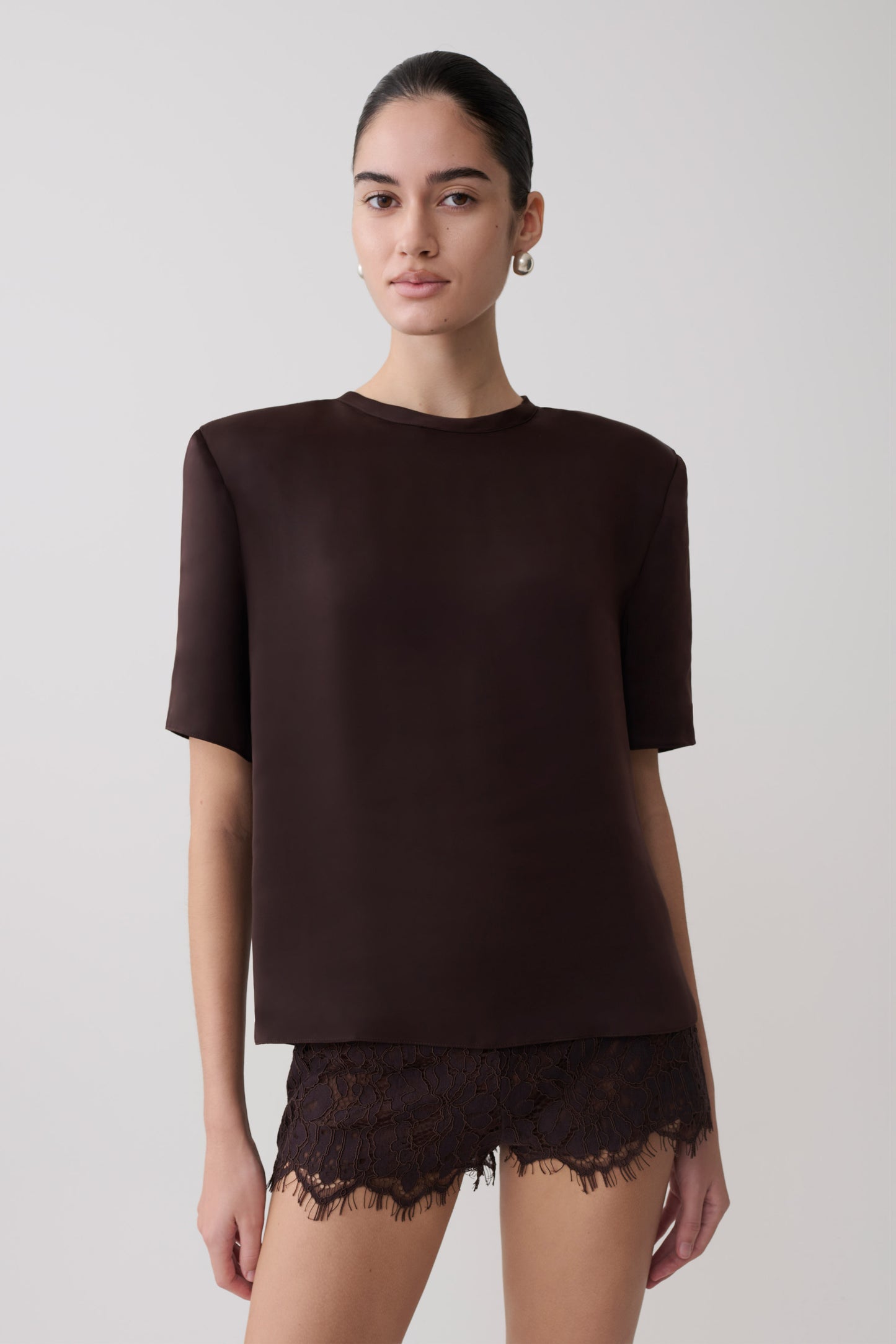Woman wearing a dark brown shoulder pad short sleeve satin top with matching lace shorts.