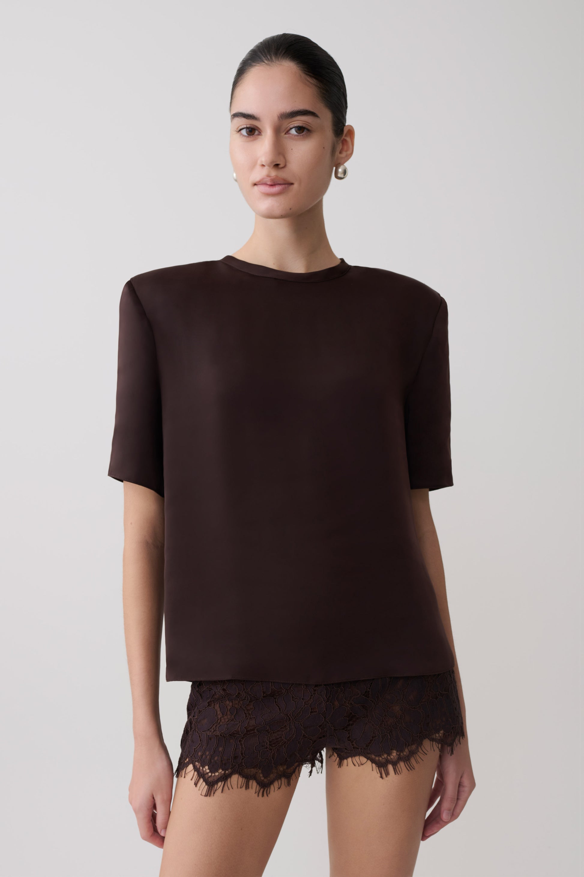 Woman wearing a dark brown shoulder pad short sleeve satin top with matching lace shorts.
