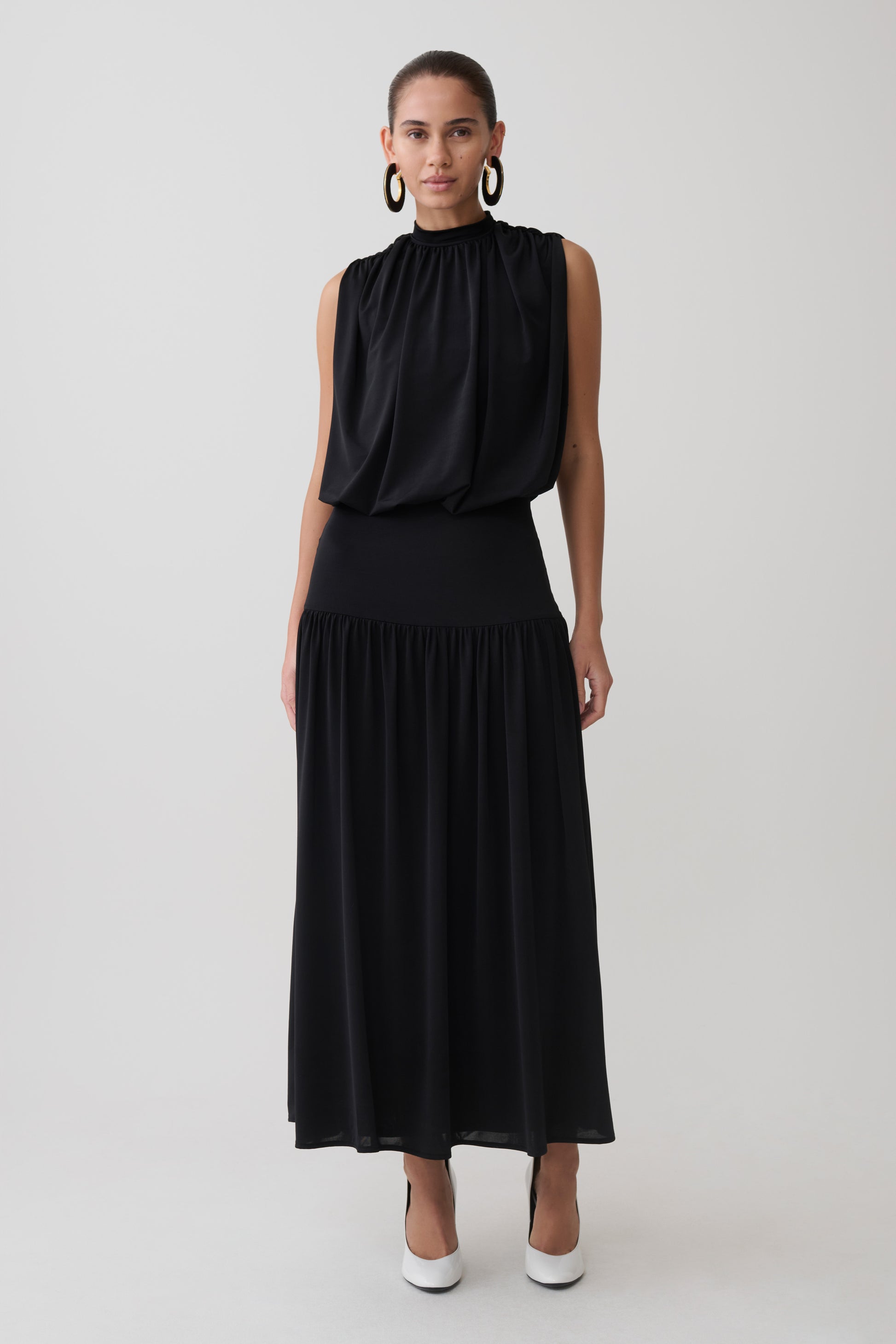 Woman wearing a black sleeveless drop waist gathered midaxi dress.