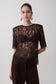 Woman wearing a dark brown shoulder pad short sleeve lace top.