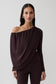 Woman wearing brown long sleeve off shoulder draped top.
