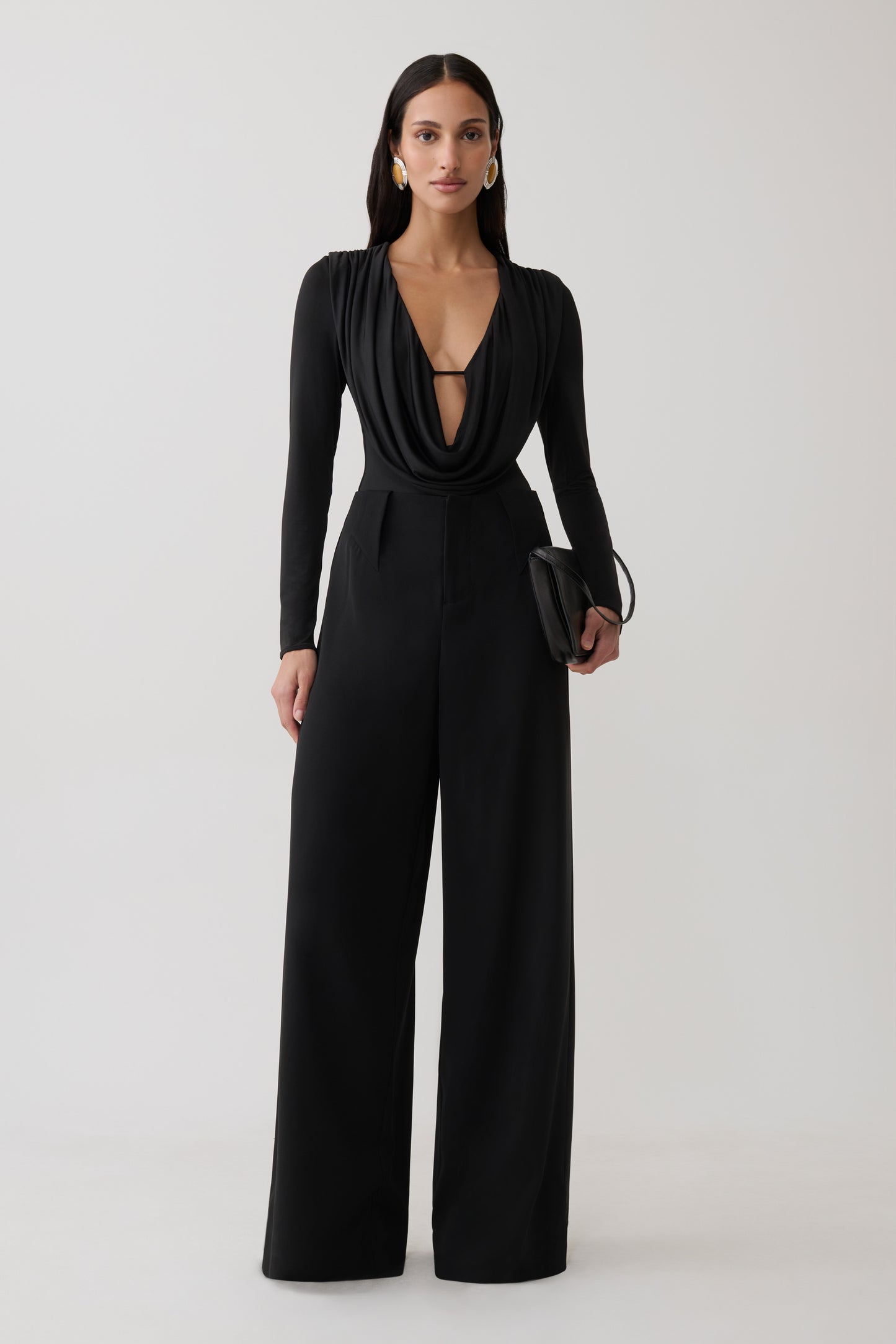 Woman wearing black cowl long sleeve slinky bodysuit, with black pants.