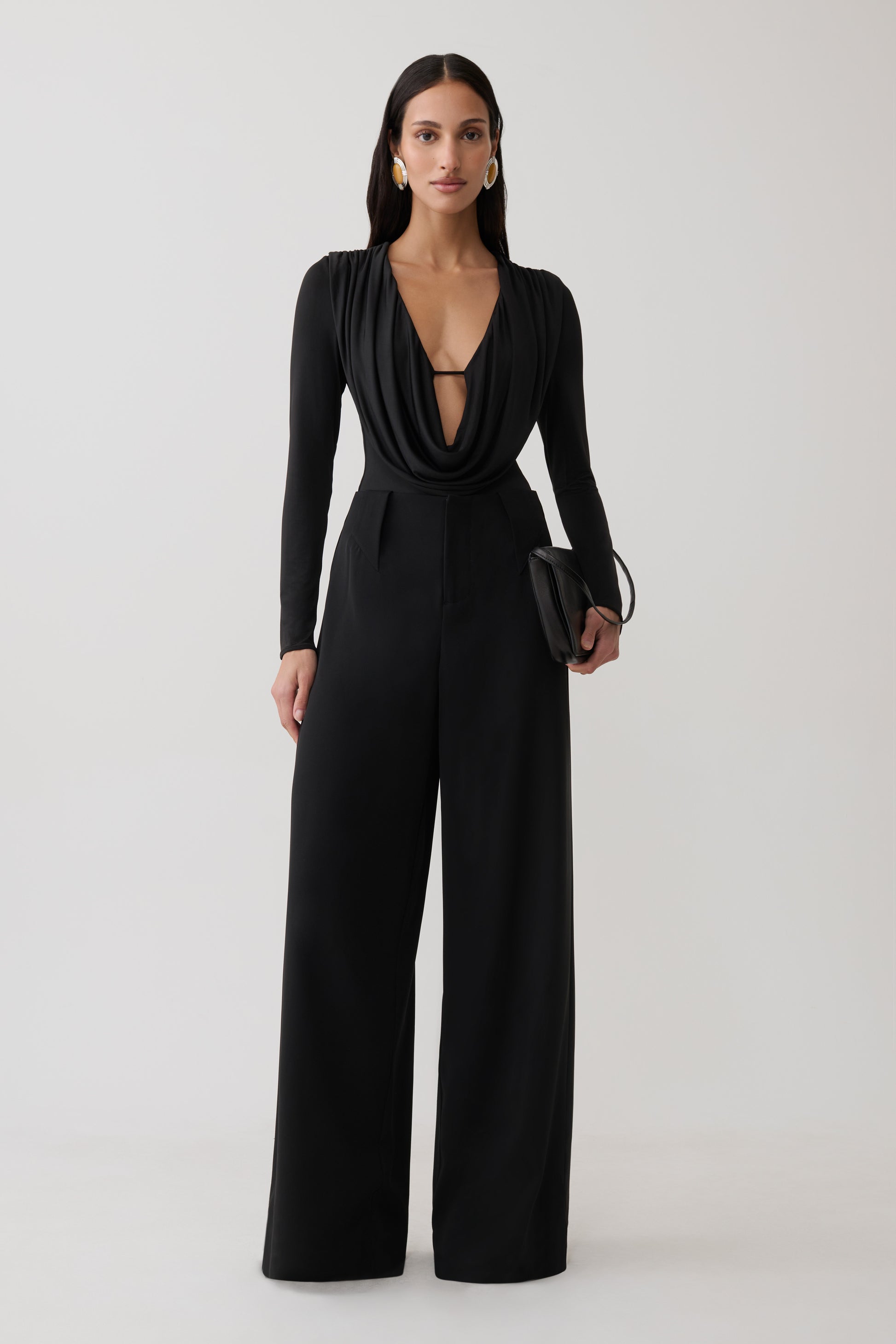 Woman wearing black cowl long sleeve slinky bodysuit, with black pants.