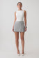 Woman wearing a white sleeveless top and grey wrap mini skirt.