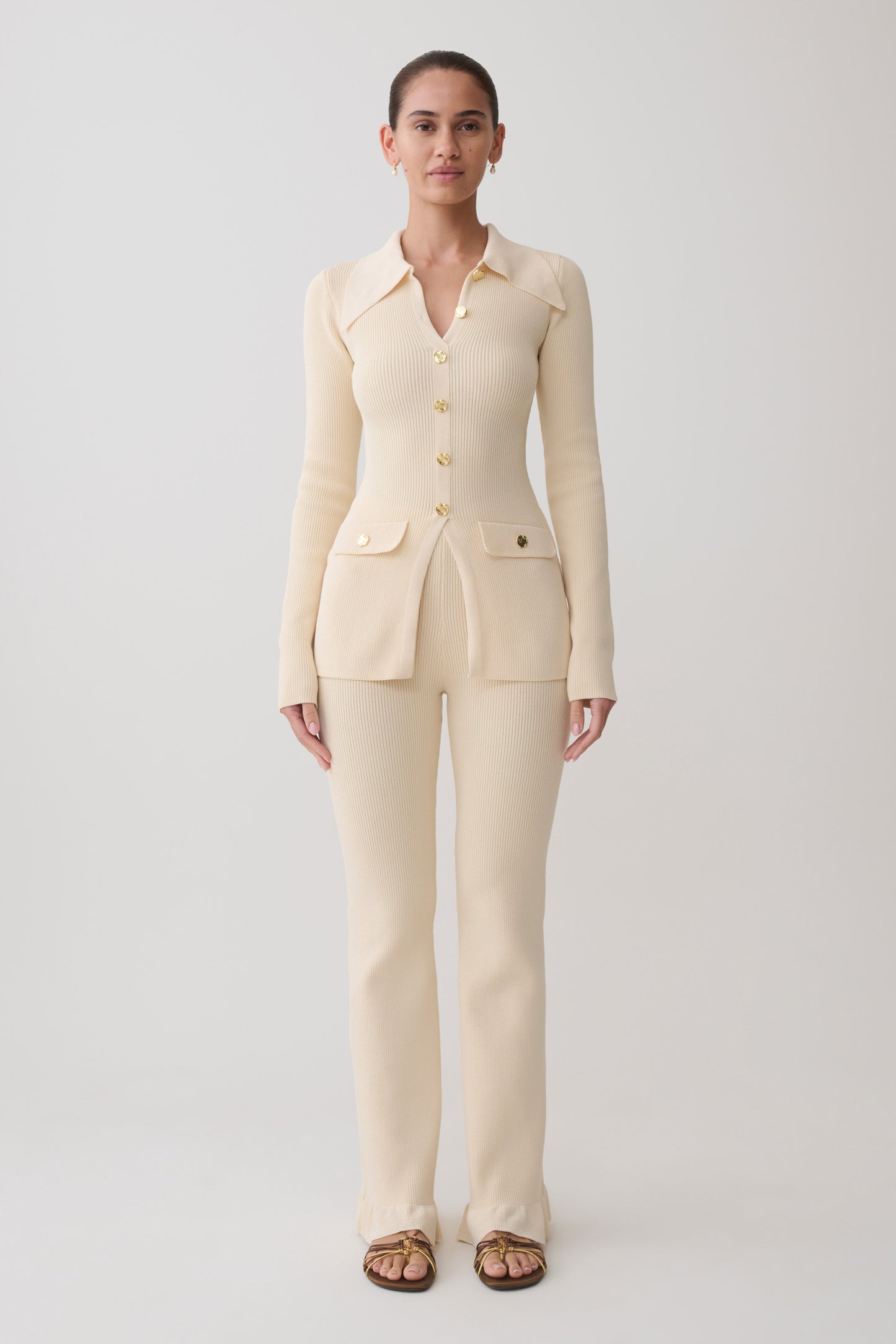 Woman wearing a white ribbed long sleeve longline top with ribbed flared pants.