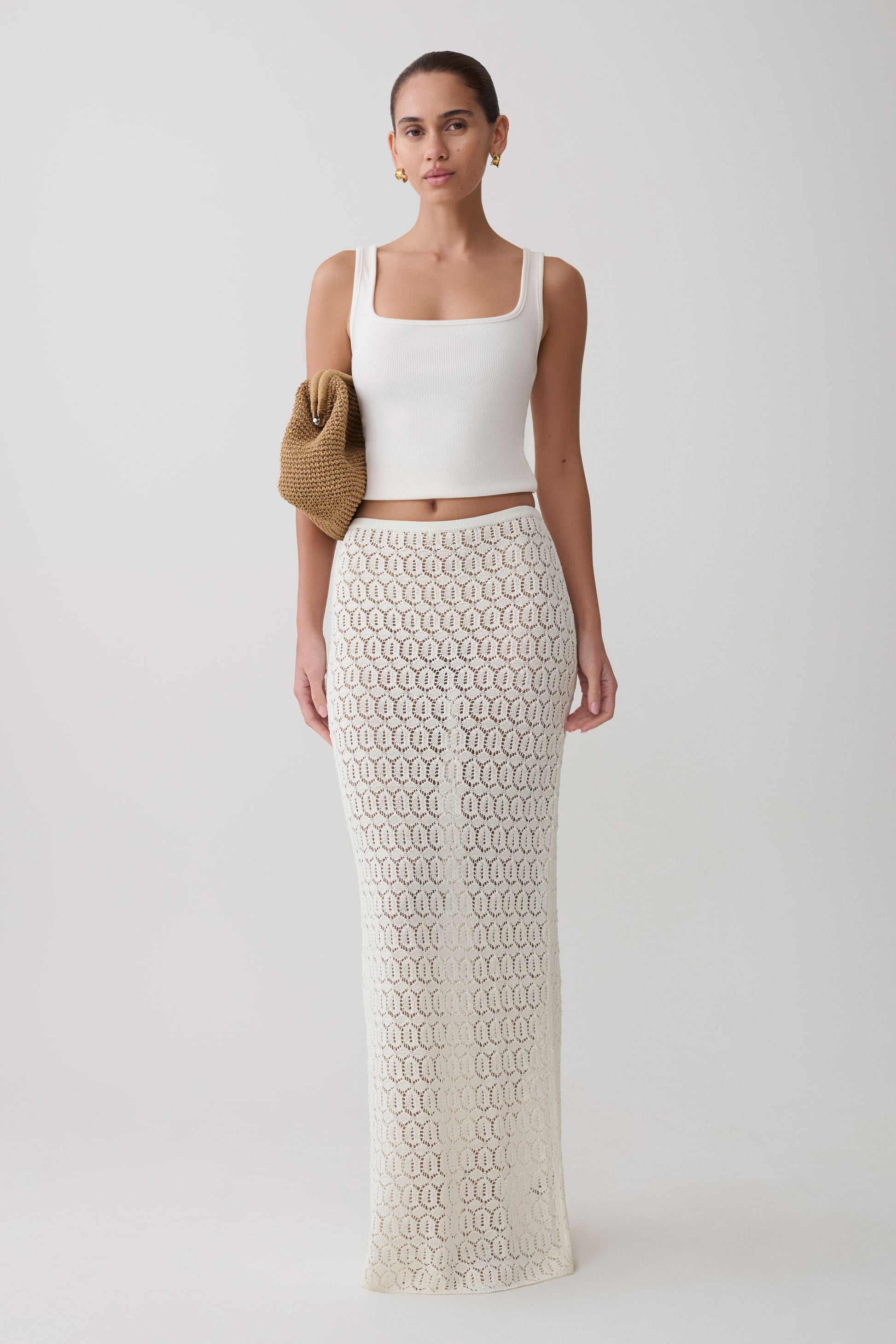 Woman wearing a white sleeveless top and white knit crochet skirt.