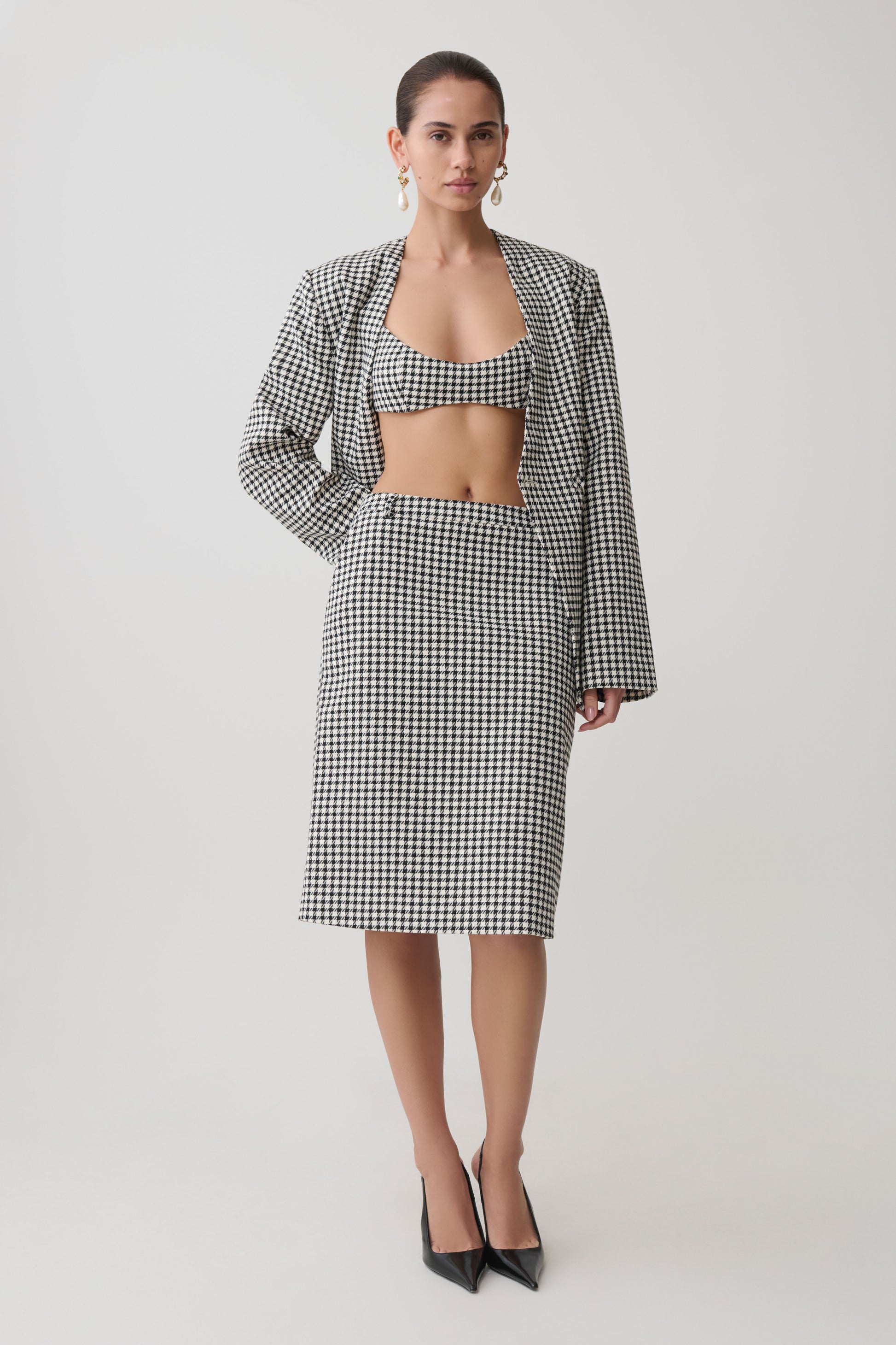 Woman wearing a black and white tweed checkered bralette with matching blazer and midi skirt.
