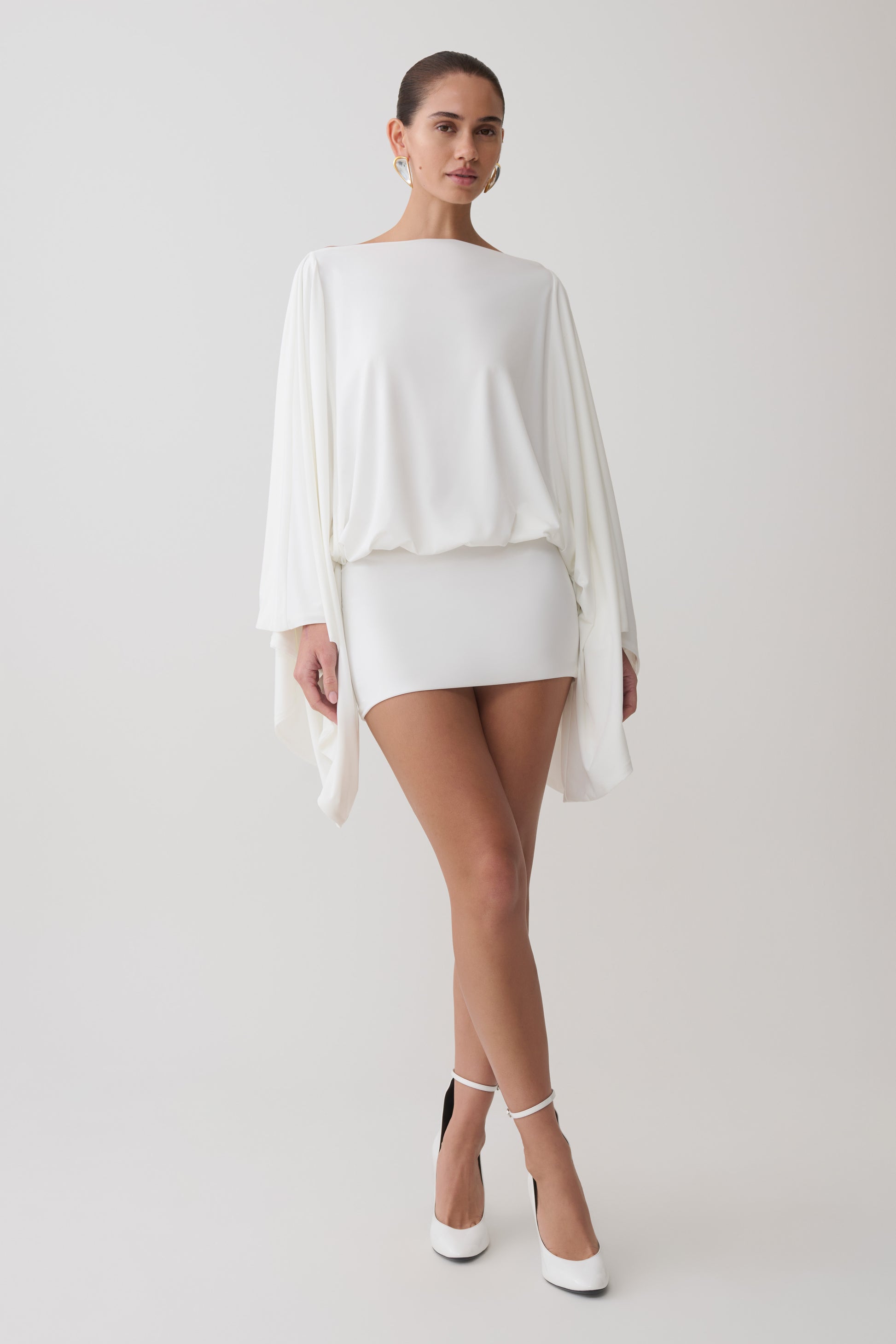 Woman wearing a white draped open back mini dress.