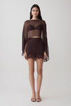 Woman wearing brown bralette with chiffon cape with matching lace and satin mini skirt.