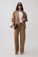 A model wearing a camel brown knit two-piece set consisting of an open-front cardigan and matching wide-leg trousers, styled with a white top, sunglasses, and a brown clutch bag against a light gray studio background.