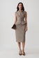 A woman models a sleeveless taupe houndstooth vest and matching pencil skirt set, holding a brown clutch against a light gray studio background.