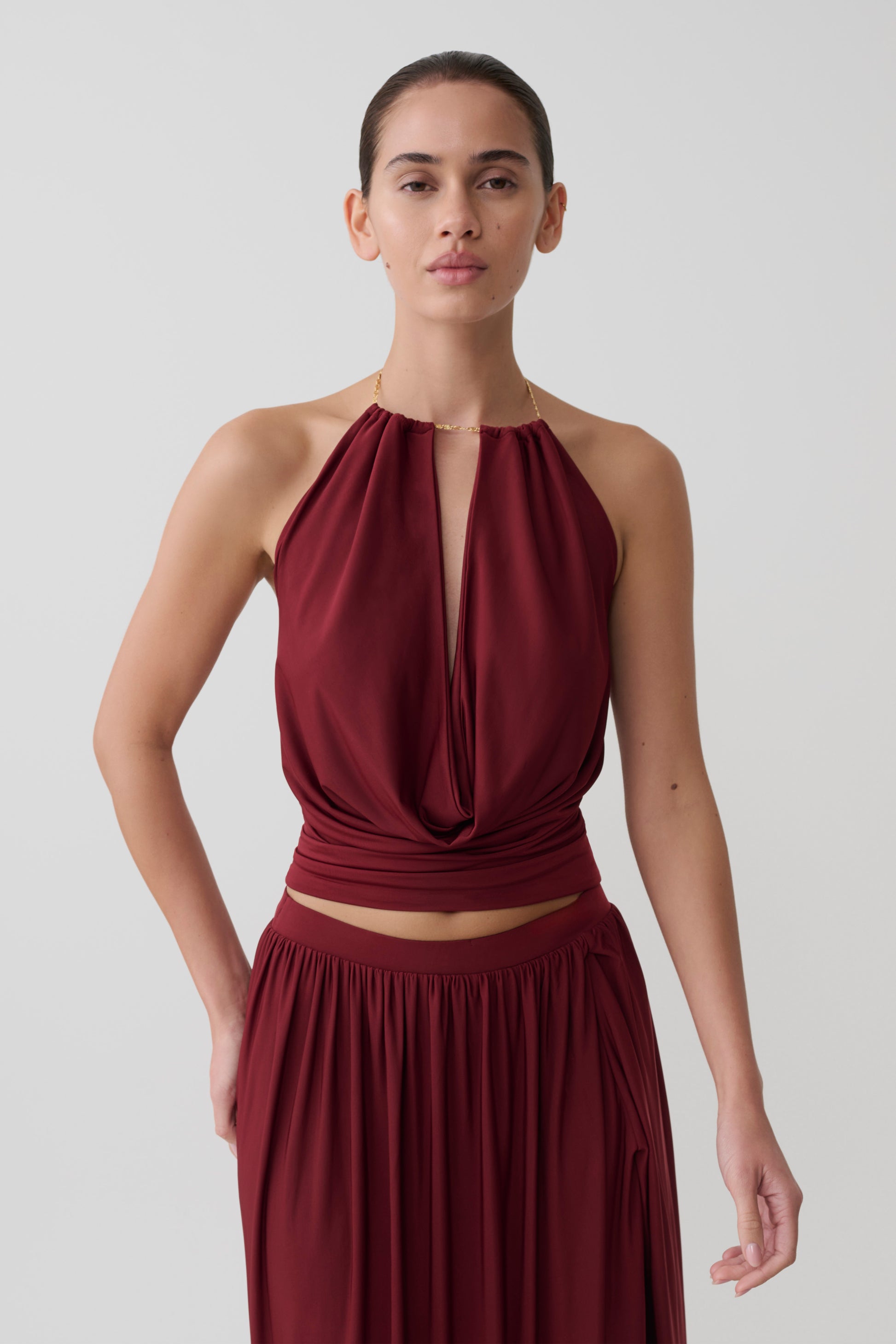 Woman wearing a dark red halter neck top with hardware.