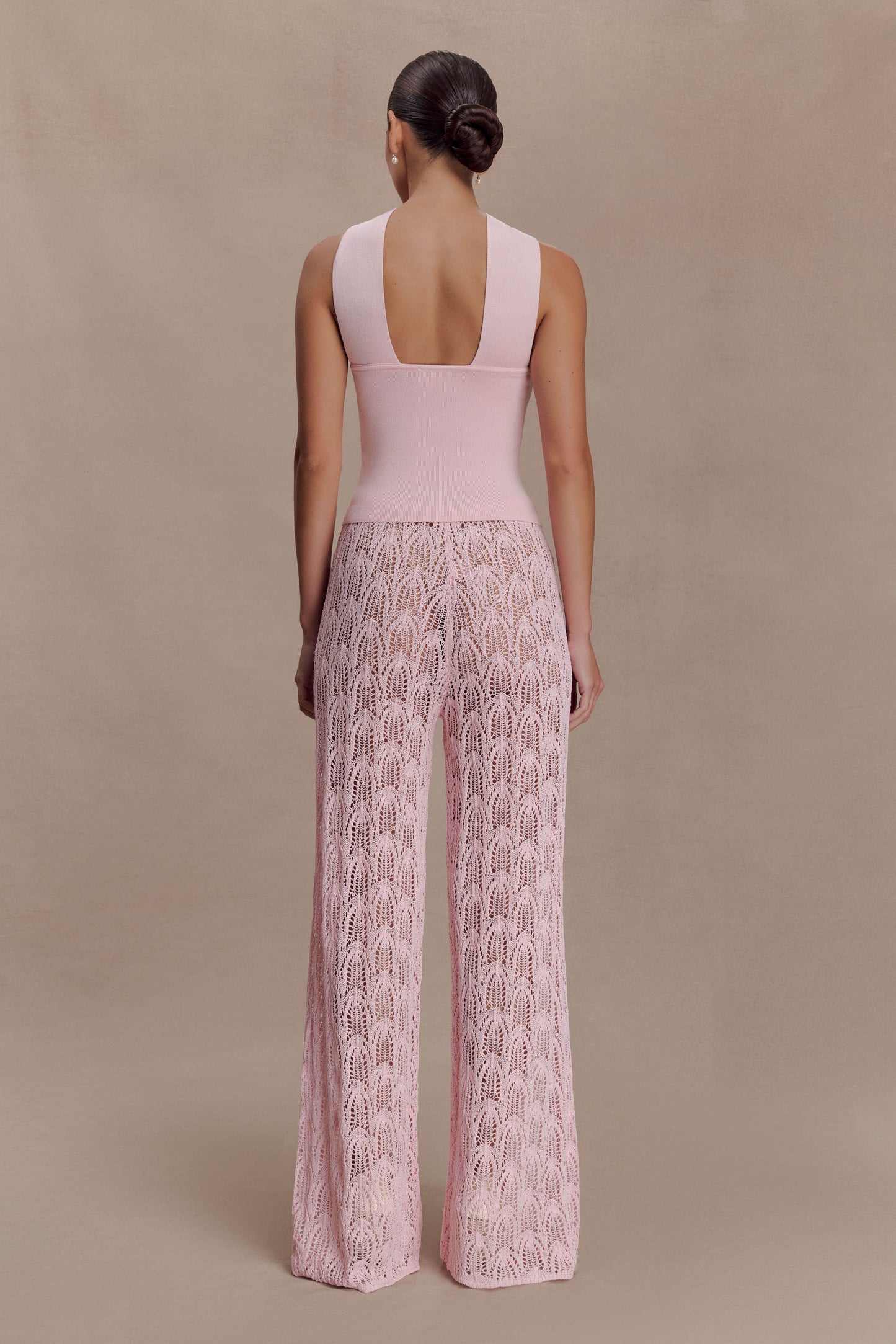 Woman wearing a pink knit top and crochet pants.