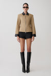 Person wearing a beige jacket with black accents, black shorts, and black knee-high boots on a white background.