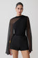 Woman wearing a black outfit with sheer sleeves on a plain background.