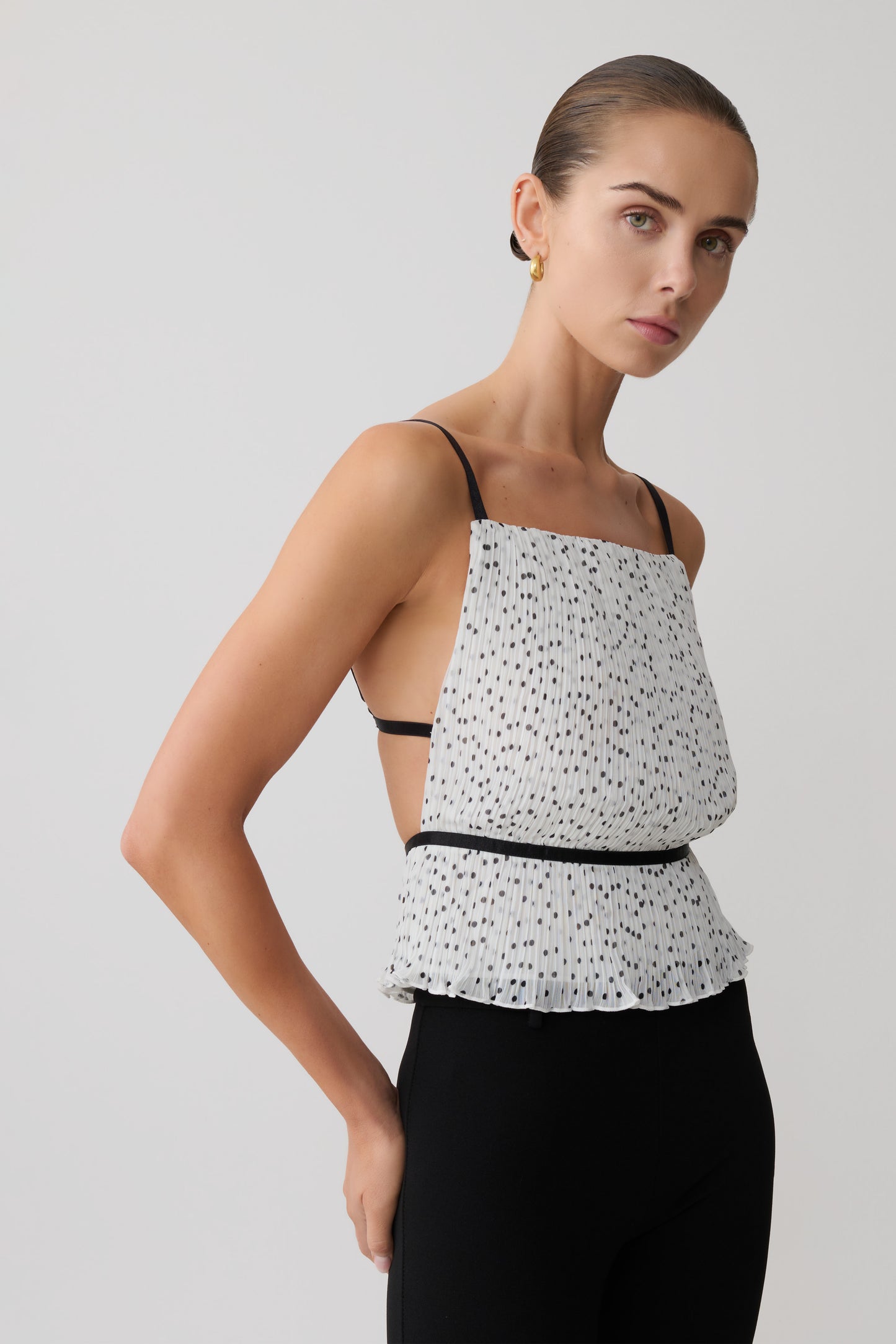 Woman wearing a pleated sleeveless polkadot top.