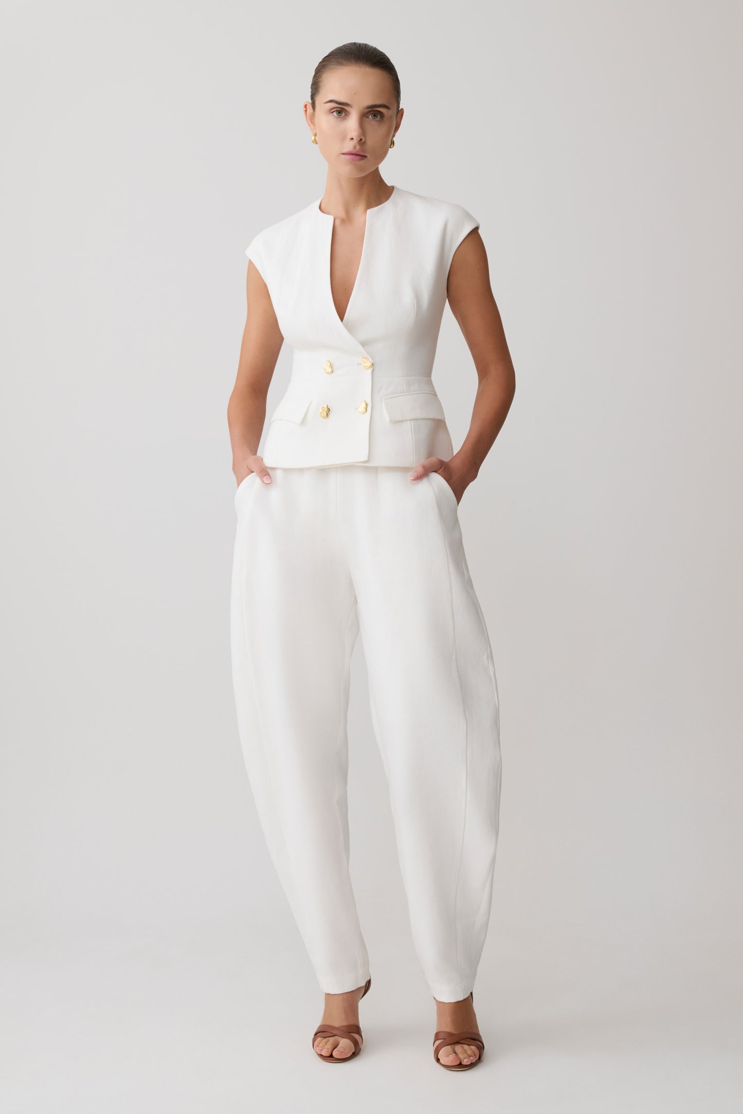 Woman wearing a white sleeveless linen vest with gold buttons with matching pants.
