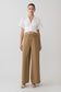 Woman wearing a white blouse and tan pants on a light gray background