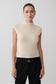 Woman wearing a beige sleeveless sweater and black pants against a plain background