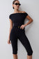Woman wearing a black off-shoulder jumpsuit with a belt against.