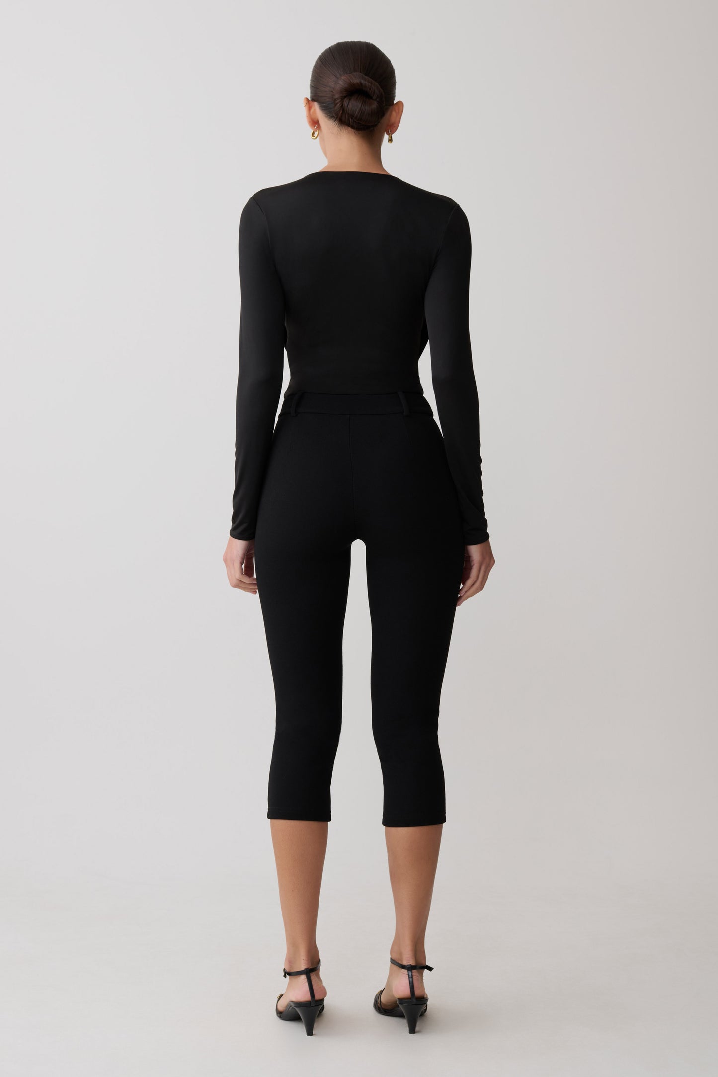 Person wearing a black long-sleeve top and capri pants on a light gray background